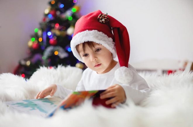 Cute adorable boy reading a book in front of the christmas tree